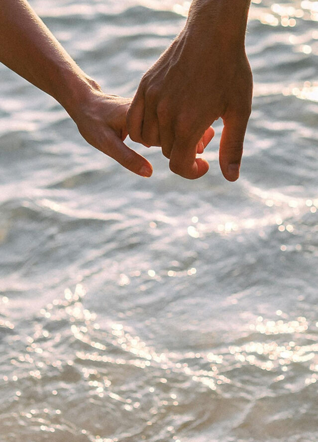 Hands held together over a sparkling water background, symbolizing connection and support for wedding planning questions.
